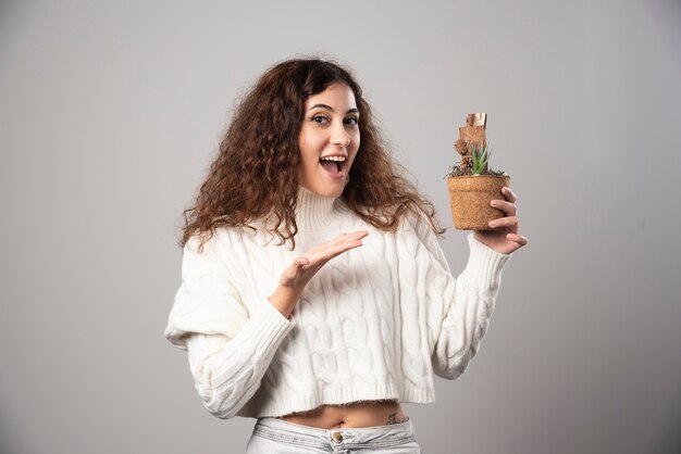 Jeune femme tenant une plante et la pointant. Photo de haute qualité