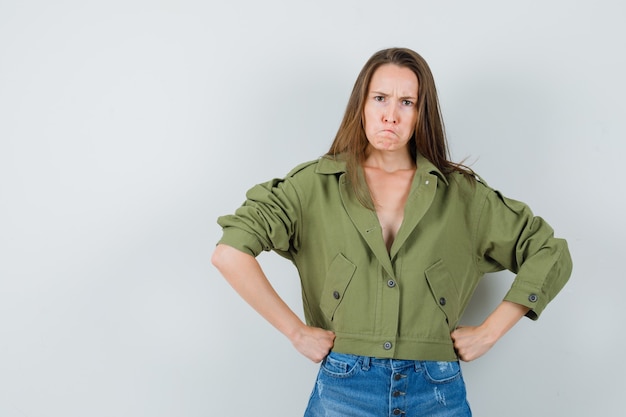 Photo gratuite jeune femme tenant les poings sur la taille en veste verte, short et à la nervosité. vue de face.