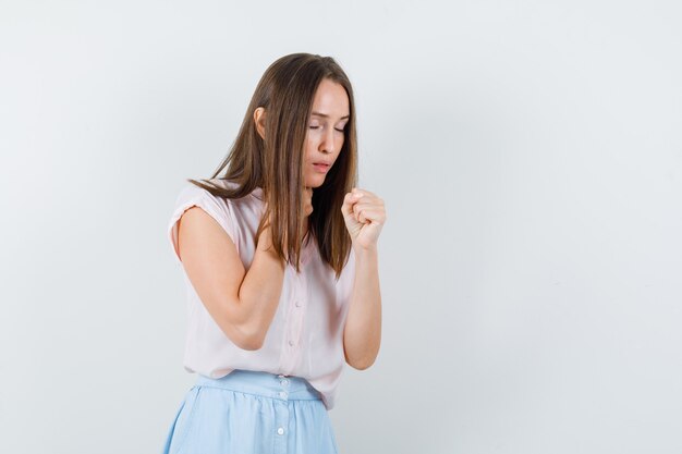 Jeune femme tenant les poings avec les yeux fermés en t-shirt, jupe et espoir, vue de face.