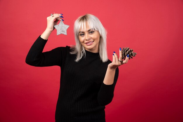 Photo gratuite jeune femme tenant une pomme de pin avec une étoile sur un mur rouge.