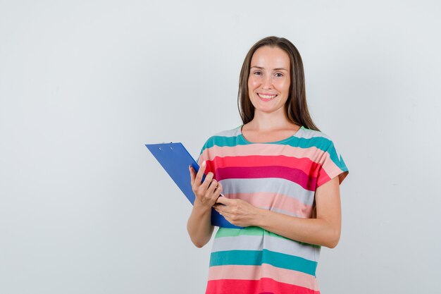 Jeune femme tenant le presse-papiers en t-shirt et l'air heureux. vue de face.
