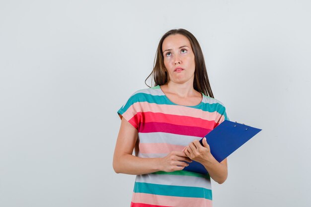 Jeune femme tenant le presse-papiers en t-shirt et à la pensif. vue de face.