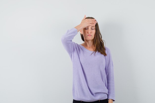 Jeune femme tenant sa main sur le front en chemisier lilas et à la recherche de stress. vue de face.