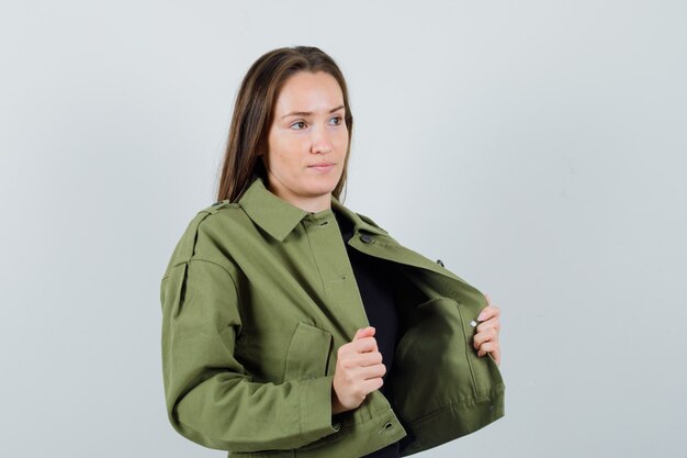 Jeune femme tenant sa veste tout en regardant de côté en vue de face de la veste verte.