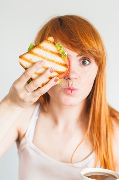 Jeune femme tenant un sandwich devant ses yeux