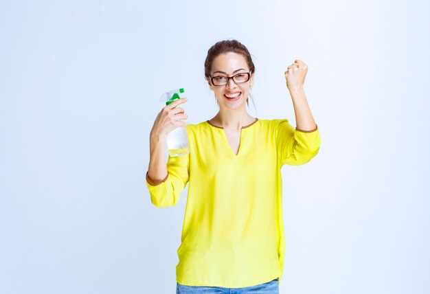 Jeune femme tenant un spray de nettoyage et montrant un signe de plaisir