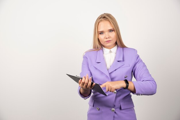 Jeune femme tenant une tablette sur un mur blanc.