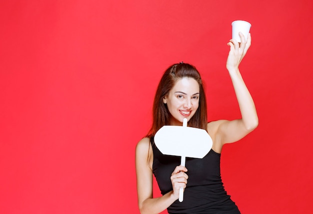 Photo gratuite jeune femme tenant une tasse de boisson jetable et un bureau d'information blanc