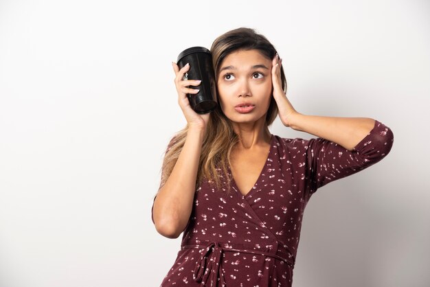 Jeune femme tenant une tasse de boisson sur un mur blanc.