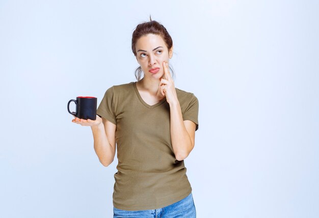 Jeune femme tenant une tasse de café noir et pensant