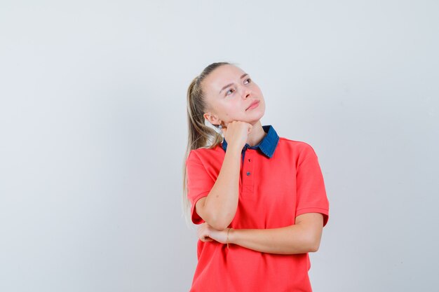 Jeune femme tenant la tête sur le poing levé en t-shirt et à la rêveuse