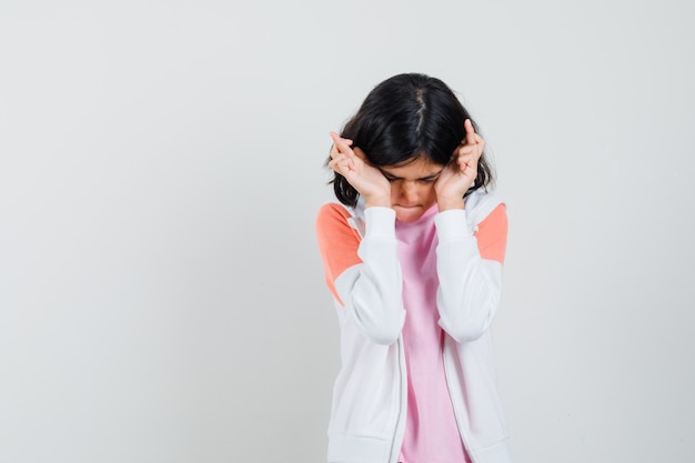 Jeune femme tenant la tête avec ses doigts croisés en veste, chemise rose et patient à la recherche.