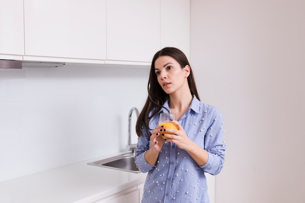 Jeune femme tenant un verre de jus debout dans la cuisine