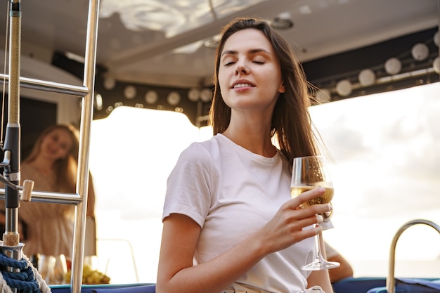 Jeune femme tenant un verre à vin et assise sur le pont du yacht à voile