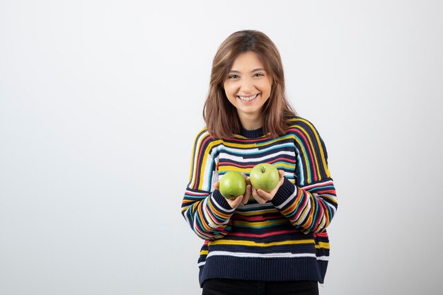 Jeune femme en tenue décontractée tenant des pommes vertes avec une expression souriante.