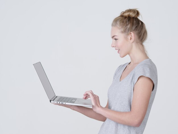 Jeune femme tient un ordinateur portable en habds. Sourire fille caucasienne avec ordinateur portable posant au studio