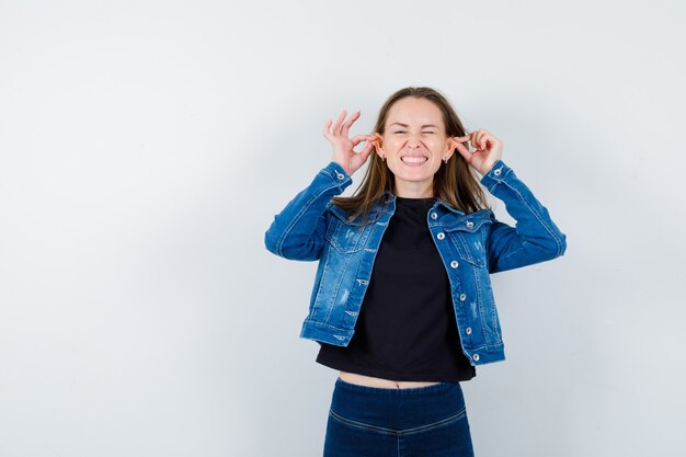 Jeune femme tirant ses oreilles en chemisier et semblant drôle.