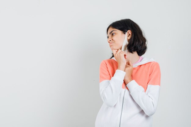 Jeune femme tirant son masque vers le bas en sweat à capuche, masque facial et l'air insatisfait.