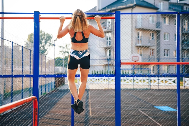 Jeune femme tirant vers le haut avec les jambes croisées sur les barres horizontales