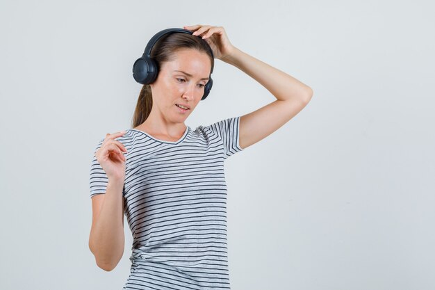 Jeune femme touchant des écouteurs en t-shirt rayé et à la pensif. vue de face.