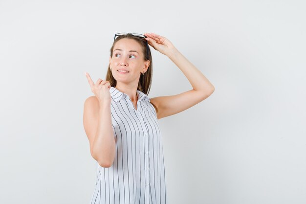 Jeune femme touchant des lunettes et pointant vers l'extérieur en vue de face de t-shirt.