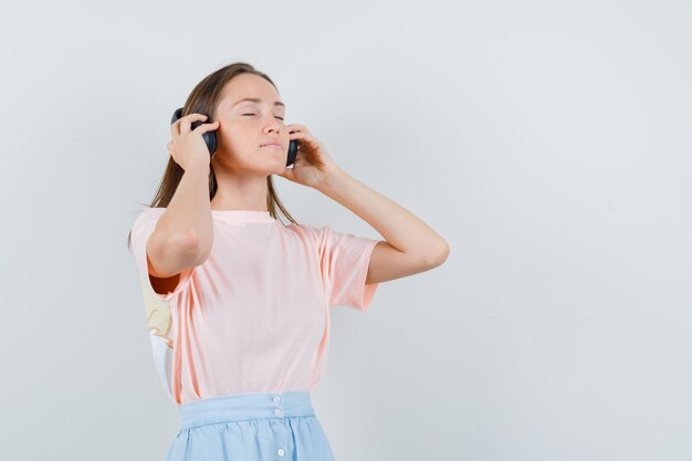 Jeune femme touchant ses écouteurs en t-shirt, jupe et à la détente. vue de face.