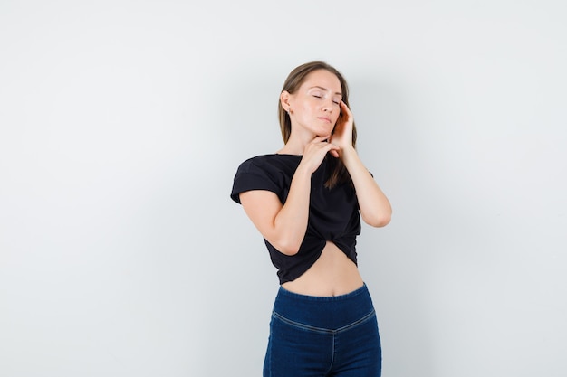 Jeune femme touchant les tempes et le menton en chemisier noir, pantalon et à la détente