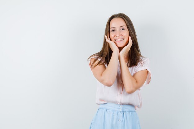 Jeune femme touchant le visage avec les mains en t-shirt, jupe et jolie vue de face.