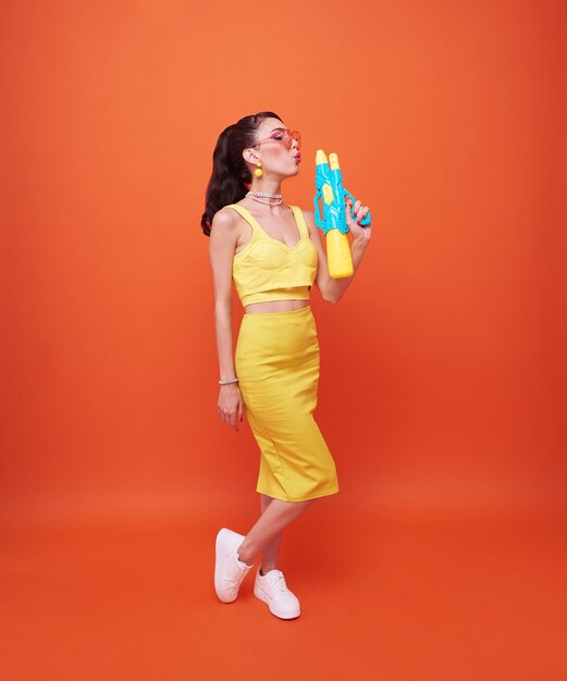 Jeune femme touriste heureuse avec un pistolet à eau pendant les vacances du festival de Songkran sur fond orange