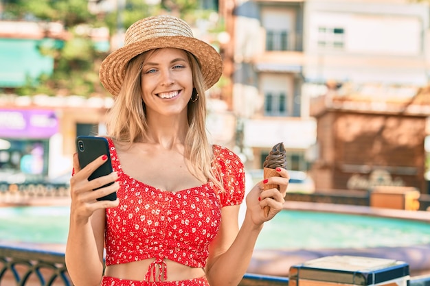 Jeune femme touristique blonde portant un style d'été à l'aide d'un smartphone mangeant des glaces à la ville