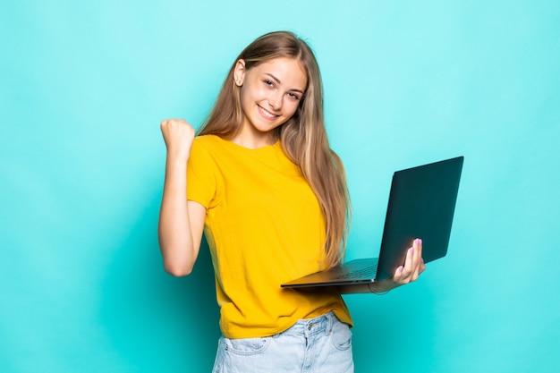 Jeune femme travaillant sur un ordinateur portable avec un geste de victoire posant isolé sur un mur turquoise