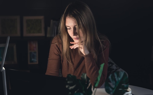 Une jeune femme travaille derrière un ordinateur portable la nuit avec une lampe