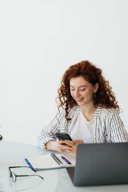 Jeune femme travailleuse assise sur le bureau et utilisant un téléphone portable