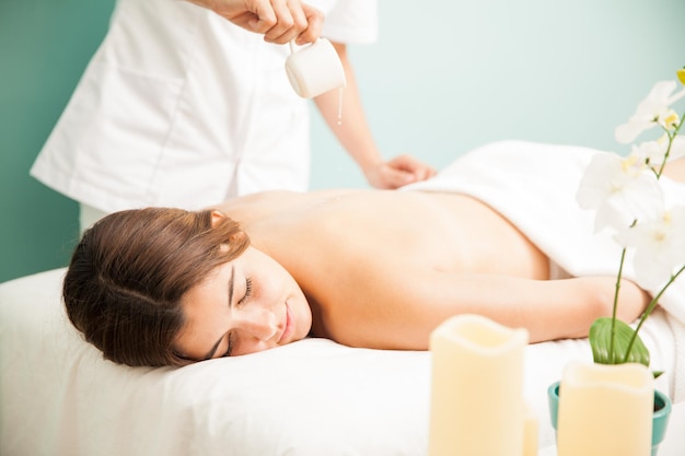 Jeune femme très détendue et mignonne recevant un massage aux bougies dans une clinique de beauté et un spa