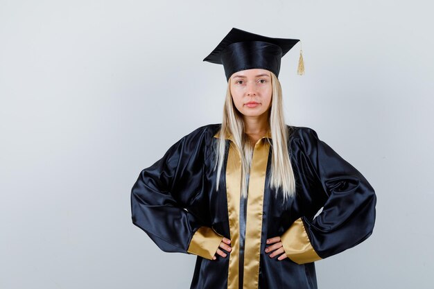 Jeune femme en uniforme diplômé gardant les mains sur la taille et ayant l'air confiant