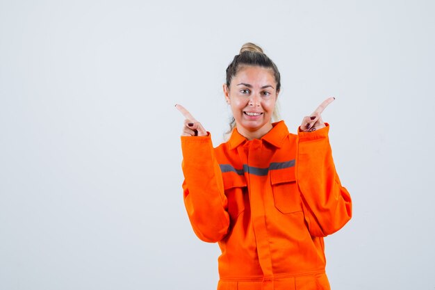 Jeune femme en uniforme de travailleur pointant sur différents côtés et à la joyeuse vue de face.