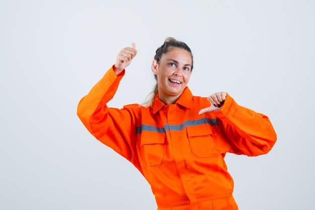 Jeune femme en uniforme de travailleur pointant de haut en bas et à la perplexité, vue de face.