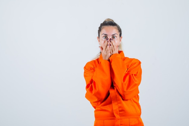 Jeune femme en uniforme de travailleur tenant la main sur sa bouche et à la peur, vue de face.