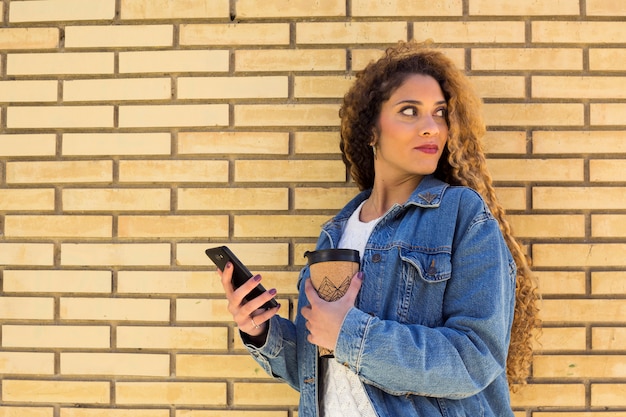 Photo gratuite jeune femme urbaine avec un smartphone devant un mur de briques