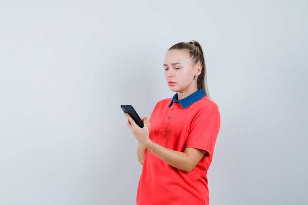 Jeune femme, utilisation, téléphone portable, dans, t-shirt, et, regarder, concerné