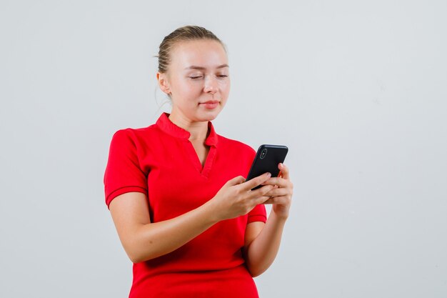 Jeune femme, utilisation, téléphone portable, dans, t-shirt rouge, et, regarder, occupé