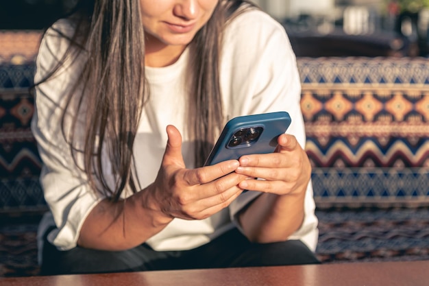 Une jeune femme utilise un smartphone assise dans un café de rue au coucher du soleil