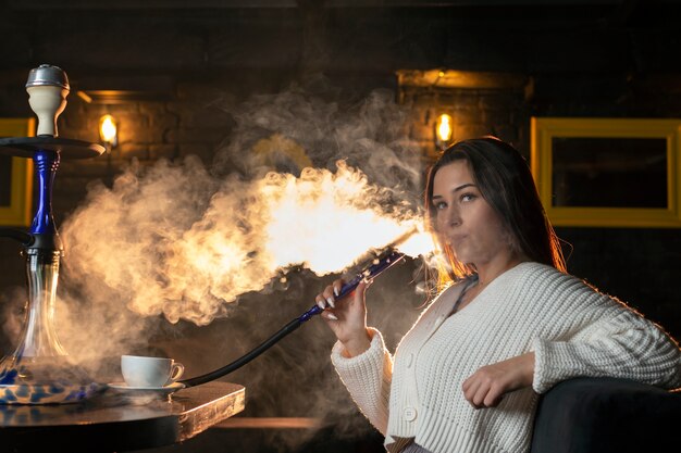 Jeune femme vapotant d'un narguilé dans un bar