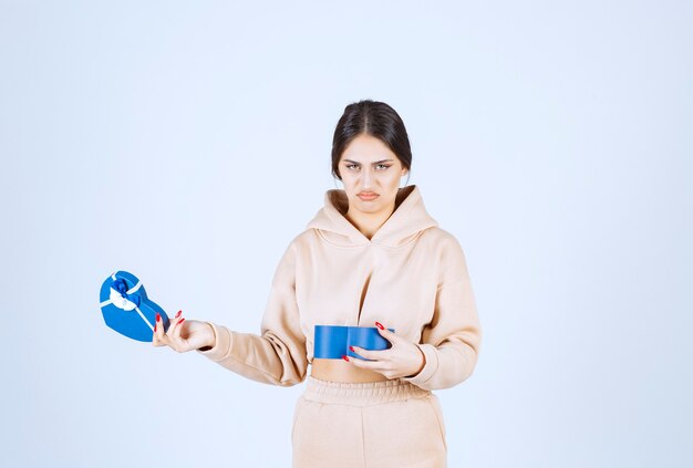 Jeune femme vérifiant la boîte cadeau bleue et semble insatisfaite