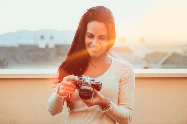 Photo gratuite jeune femme vérifiant son appareil photo vintage au coucher du soleil