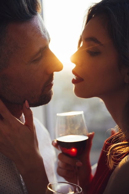 Photo gratuite jeune femme avec verre de vin embrassant son homme au coucher du soleil