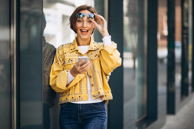 Jeune femme en veste jaune à l'aide de téléphone à l'extérieur dans la rue