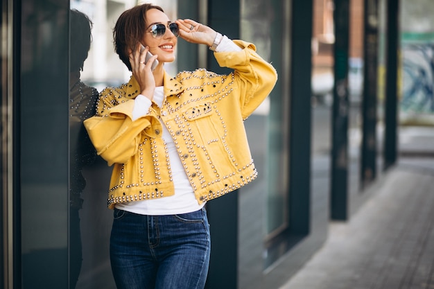 Photo gratuite jeune femme en veste jaune à l'aide de téléphone à l'extérieur dans la rue