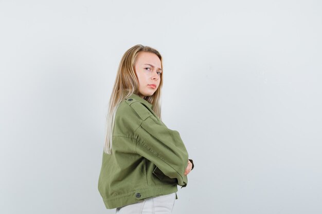 Jeune femme en veste, pantalon debout avec les bras croisés et à la recherche du doute.