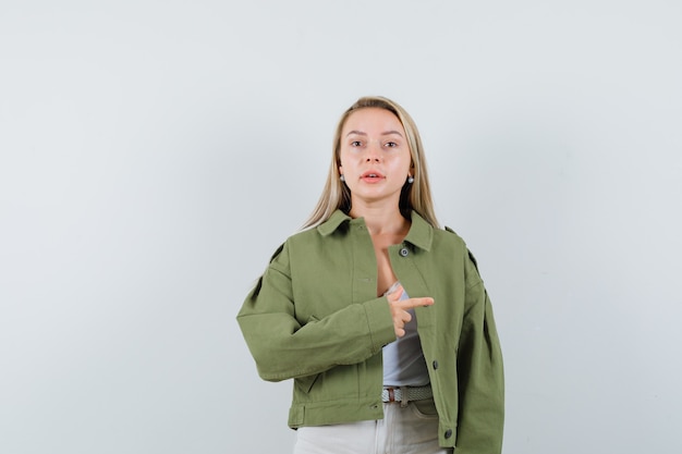 Jeune femme en veste, pantalon pointant vers le côté droit et regardant confiant, vue de face.